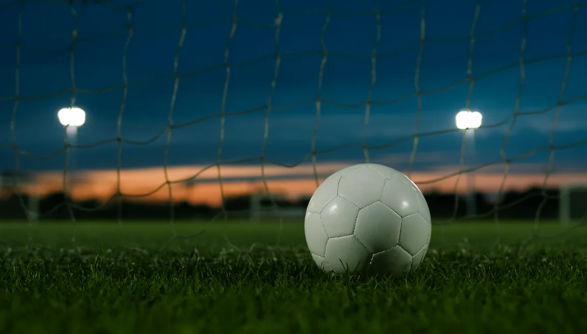 A football in front of a goal net at dusk
