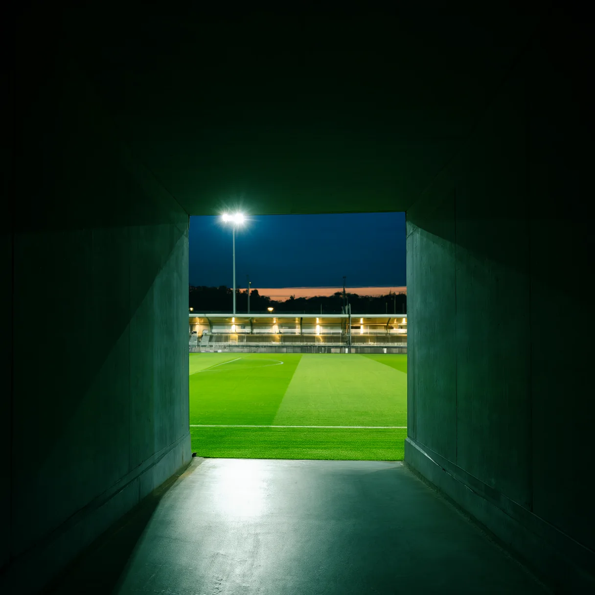 The players’ tunnel opening onto a floodlit pitch at dusk